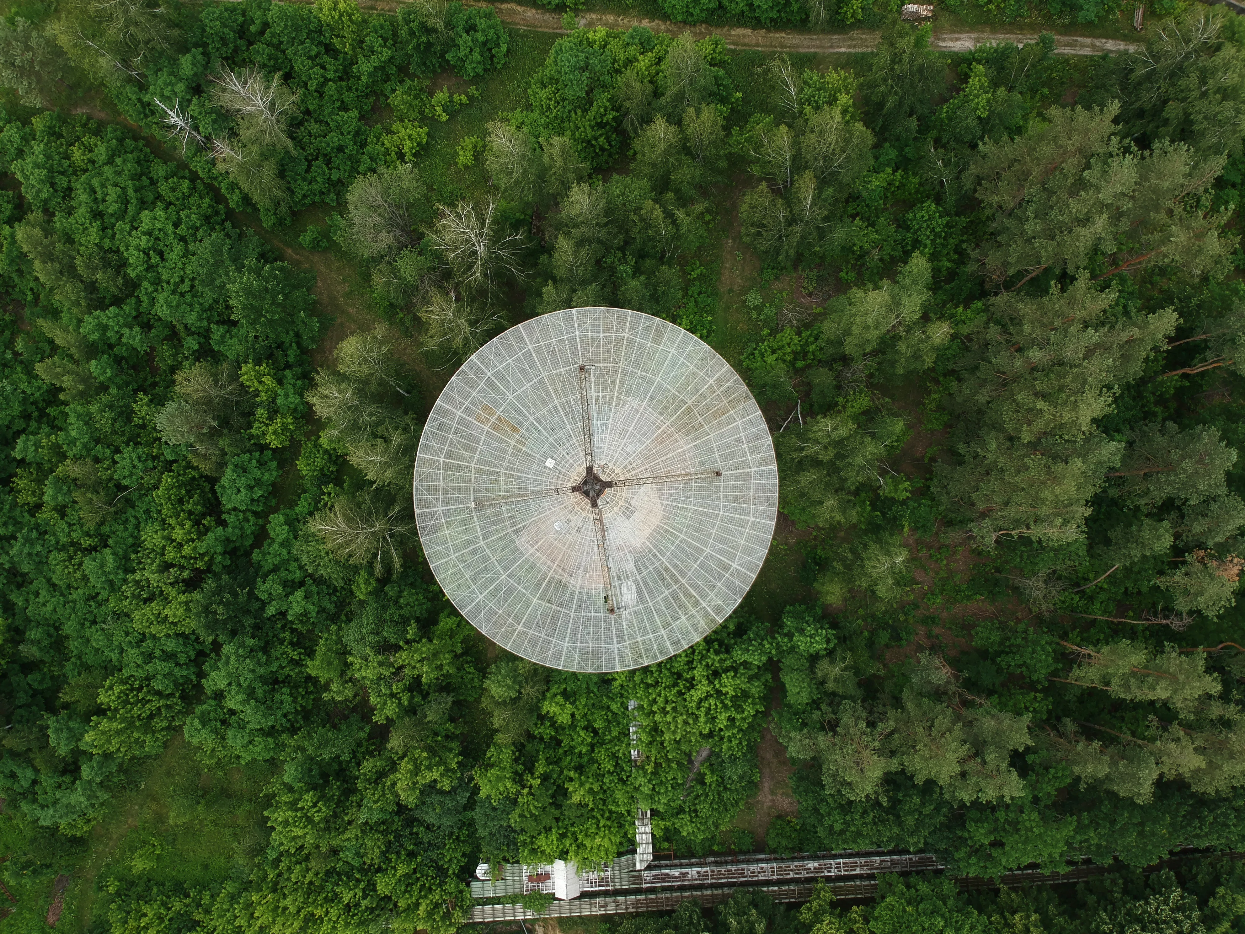 Vista aérea de una gran antena parabólica en un bosque, utilizada para comunicación y sistemas GPS satelital.
